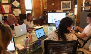 6 people seated at table with laptops
