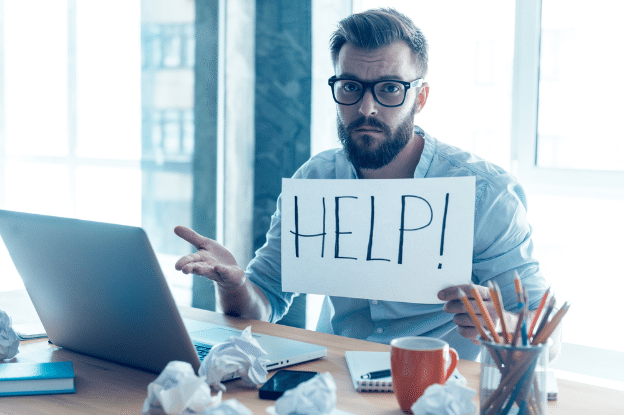 Man with laptop computer holding up a card that says help in black marker