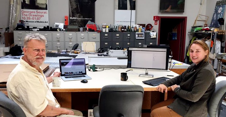 Two smiling people sitting at a table with computers