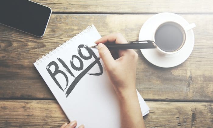 woman writing blog on notebook and coffee and phone on table