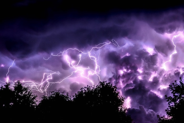 Lightning in a purple sky over trees