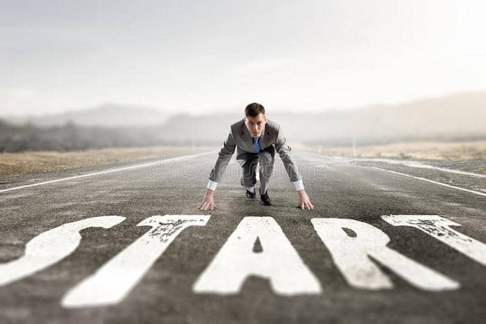 Man in a starting running position behind the word Start on the road 