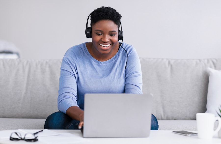 Black woman sitting on couch, virtual training on laptop