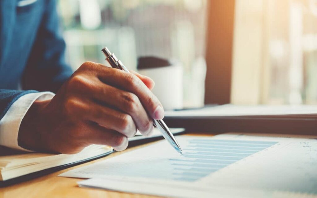 hand with pen pointing to a paper with a graph